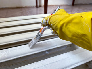 Worker painting old radiator with white paint using brush
