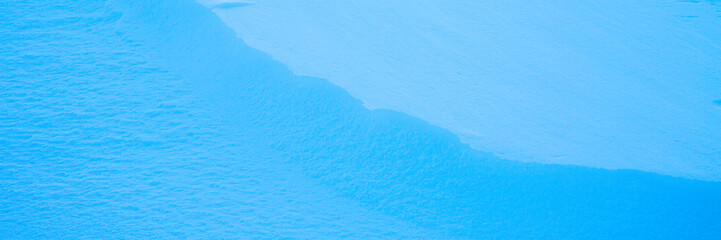 Beautiful winter background with snowy ground. Natural snow texture. Wind sculpted patterns on snow surface. Wide panoramic texture for background and design. Closeup top view with copy space.