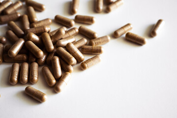 Brown herbal capsules close up scattered on white background for healthcare