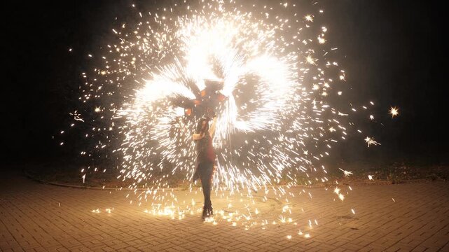 A night performance with fireworks. A woman dances with fire ropes, launching fireworks. The circus performer throws fire sparks, creating an impressive and beautiful performance in slow motion.