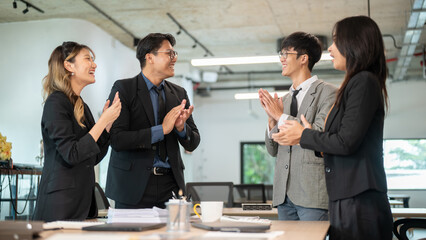Smiling businessman and woman clapping hands with coworkers at wooden table after meeting in office