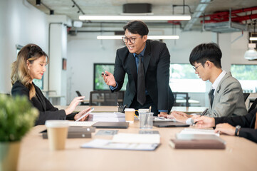 Happy businessman standing and talking to woman coworker holding tablet at wooden table in office.