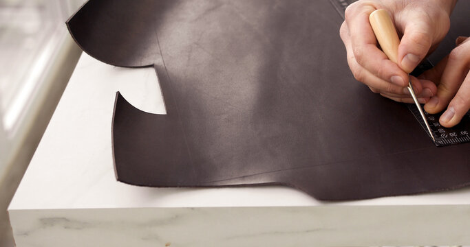 Close-up of craftsman marking leather with ruler and awl for handmade leatherwork