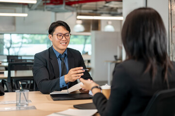 Businessman holding pen over notebook talking with woman coworker at wooden table in meeting room