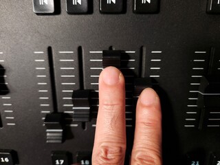 Close-up of a person's hand adjusting sliders on a lighting control console used in stage.