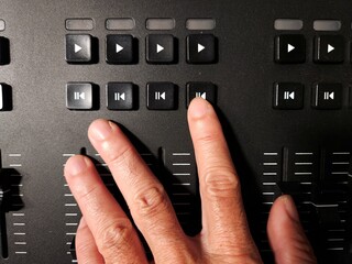 Close-up of a person's hand adjusting sliders on a lighting control console used in stage.