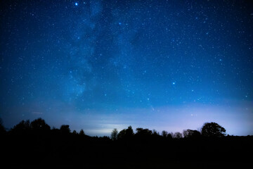 Milky Way stars with countryside tree and landscape silhouettes.