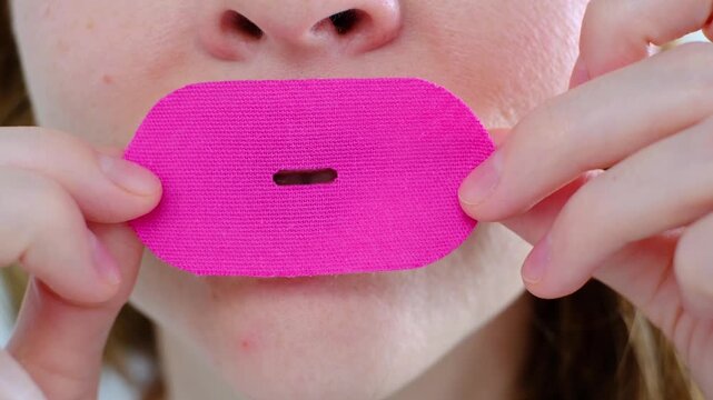 A girl puts a snoring patch on her mouth, close-up to sleep with her mouth closed and breathe through her nose. Healthy sound sleep with proper breathing. The toned oval of the face. Wellness