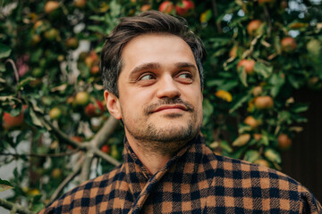 stylish European man in a vintage brown wool blazer stands contemplatively by an apple tree