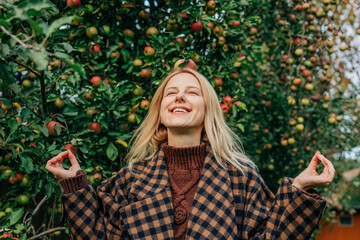 European woman stands by an apple tree in an autumn orchard, playfully balancing a ripe red apple on her head