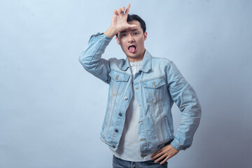 Obraz premium Asian man in denim jacket sticking out his tongue while making an 