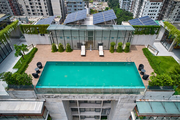 High-angle shot of a modern rooftop pool with wooden deck, lounge chairs, and solar panels, framed by the surrounding city buildings. Perfect for themes of urban living and modern architecture.