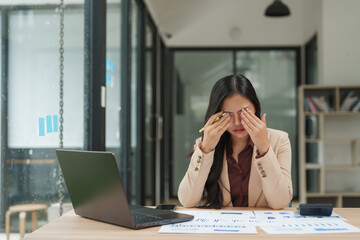 Stressed asian businesswoman rubbing eyes at office desk