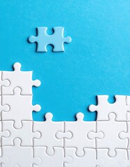 Obraz premium A single light-blue jigsaw puzzle piece sits atop a partially completed white jigsaw puzzle against a vibrant, light-blue background