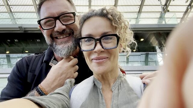 Happy middle-aged couple taking video selfie or making video call in train or metro station, travelers enjoying journey, love, connection, modern lifestyle, commuting or tourism moments