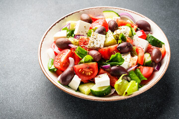 Greek salad in craft plate on black kitchen table.