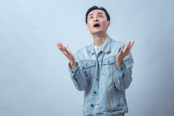 Asian man in denim jacket screaming with both hands raised, expressing anger, frustration, sadness,...