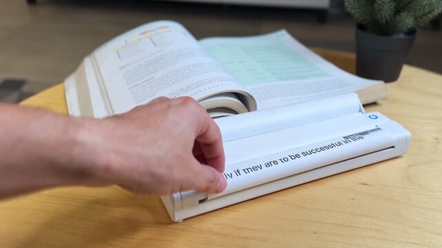 Closeup of hand scanning printed document with portable scanner on desk. Perfect for business, education, office, research, digital workflow, and productivity projects.