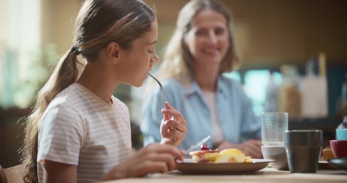 Mother and Daughter Enjoy a Sunny Breakfast, Discussing School and Cooking Tips. Cheerful Family Time for  Learning Healthy Habits Together. Slow motion