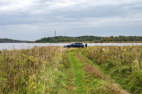 Autumn landscape with off-road car on riverbank. The man is taking by phone near the car. - Powered by Adobe