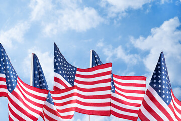 Waving United States flags on bright sky backdrop, symbol of liberty and democracy. Background for...