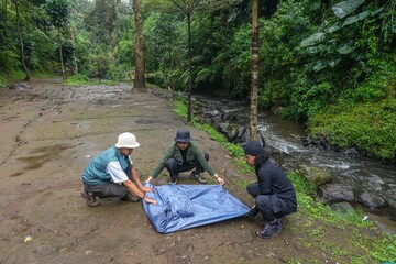 Fototapeta premium Three Friends Preparing Tent Near Stream In Lush Green Forest
