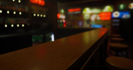 A close up view of a polished wooden bar top in a cozy establishment. Soft lighting casts a warm glow, enhancing the nostalgic retro signage in the background.