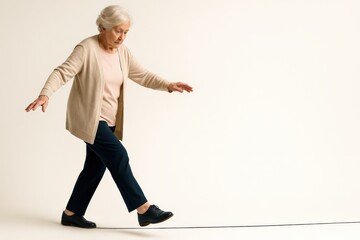An elderly woman practicing her balance while walking on a tightrope, showcasing determination and focus in pursuit of improved physical health and wellness.