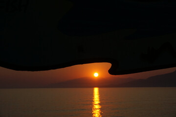 Tramonto del sole sul mare, con riflesso sulle onde, il tutto contornato da un pannello pubblicitario ondulato