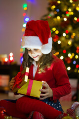 Little girl dressed as Santa Claus opens a present on Christmas at home.