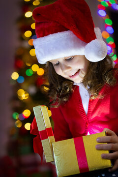 Little girl dressed as Santa Claus opens a present on Christmas at home.