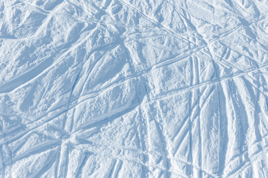 Snowy abstract off-piste skiing background with ski and snowboard trails and tracks on new virgin powder snow. morning sunrise or evening sunset time at alpine mountain resort