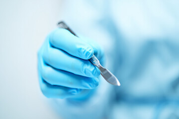 Gloved hand holds surgical scalpel in clinical setting, symbolizing precision, hygiene, and medical procedure readiness.