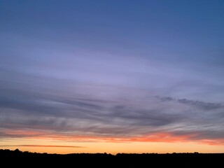 Beautiful colorful sunset sky with vibrant orange and purple clouds above dark forest silhouette