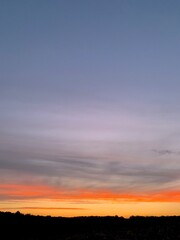 Beautiful colorful sunset sky with vibrant orange and purple clouds above dark forest silhouette