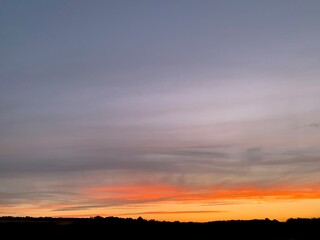 Beautiful colorful sunset sky with vibrant orange and purple clouds above dark forest silhouette