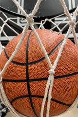 Close-up of an orange basketball falling through a basketball hoop and a white nylon net