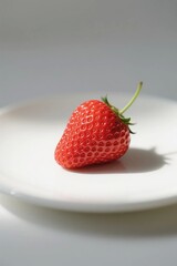 A single fresh red strawberry placed on a white plate