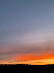 Obraz premium Beautiful colorful sunset sky with vibrant orange and purple clouds above dark forest silhouette