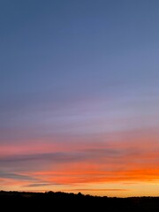 Beautiful colorful sunset sky with vibrant orange and purple clouds above dark forest silhouette
