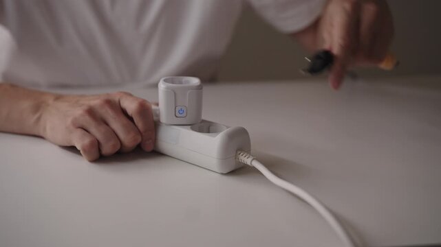 Close-up of unrecognizable man plugging smart plug into white extension cord on table. Concept of smart home technology and energy management. Shooting in slow motion.
