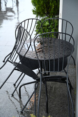 Rain-soaked caf&eacute; tables and chairs abandoned under gray skies in an urban setting