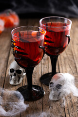 Halloween spooky red cocktail in skeleton hand glass on rustic wooden table
