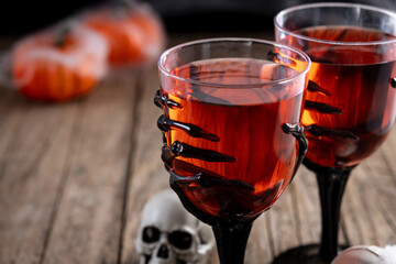 Halloween spooky red cocktail in skeleton hand glass on rustic wooden table. Copy space