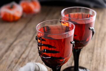 Halloween spooky red cocktail in skeleton hand glass on rustic wooden table. Copy space