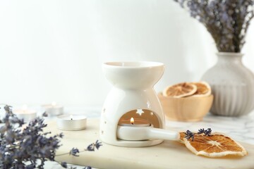 Aroma lamp with burning candle, lavender and dry orange slices on white table, closeup