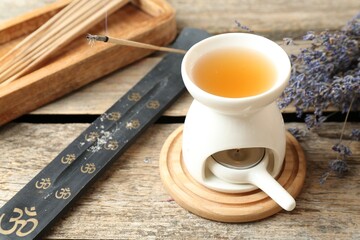Aroma lamp with burning candle, smoldering incense stick and lavender on wooden table, closeup