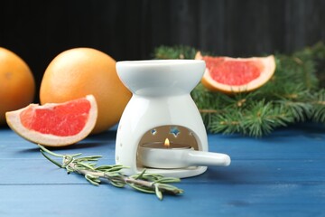 Aroma lamp with burning candle, rosemary, grapefruits and fir tree branches on light blue wooden...