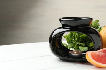 Aroma lamp with burning candle, mint leaves and grapefruits on white wooden table against grey...