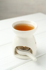 Aroma lamp with burning candle on white wooden table against grey background, closeup